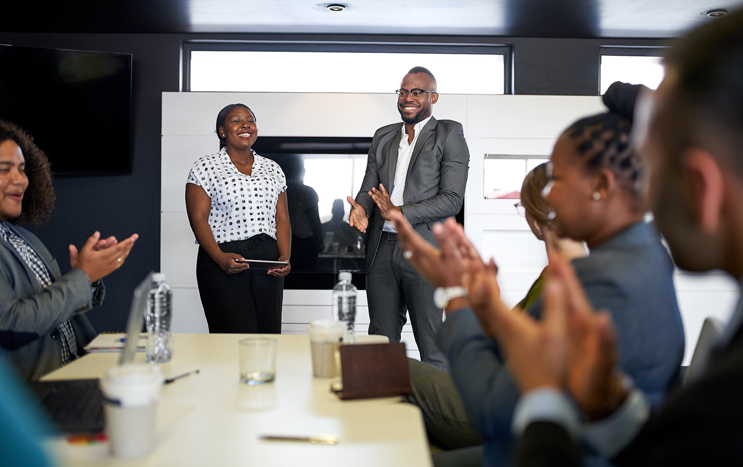 Group of mixed race colleagues in modern meeting room with laptop computer encouraging two attractive African American business professionals leading a collaborative discussion